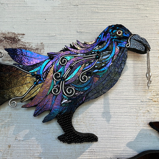 Shattered glass on wood in a light catching array, in the shape of a raven with bauble.